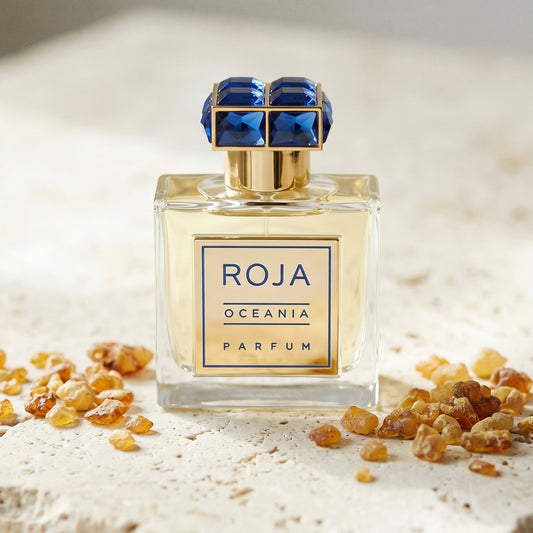 Roja Oceania Parfum on cream stone with a scatter of honey-colored ambergris flakes