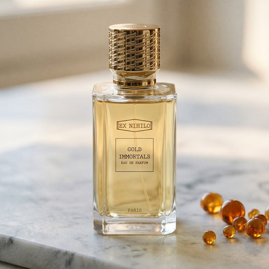 Ex Nihilo Gold Immortals EDP on pale grey marble with amber resin beads scattered to one side