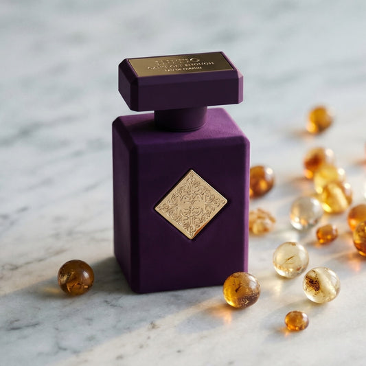 Initio Can't Get Enough EDP on pale grey marble with amber resin beads scattered to one side