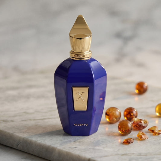 Xerjoff Accento EDP on pale grey marble with amber resin beads scattered to one side