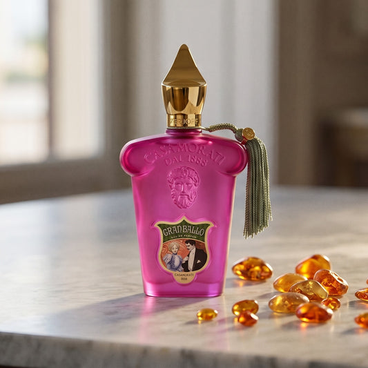 Xerjoff Gran Ballo EDP on pale grey marble with amber resin beads scattered to one side