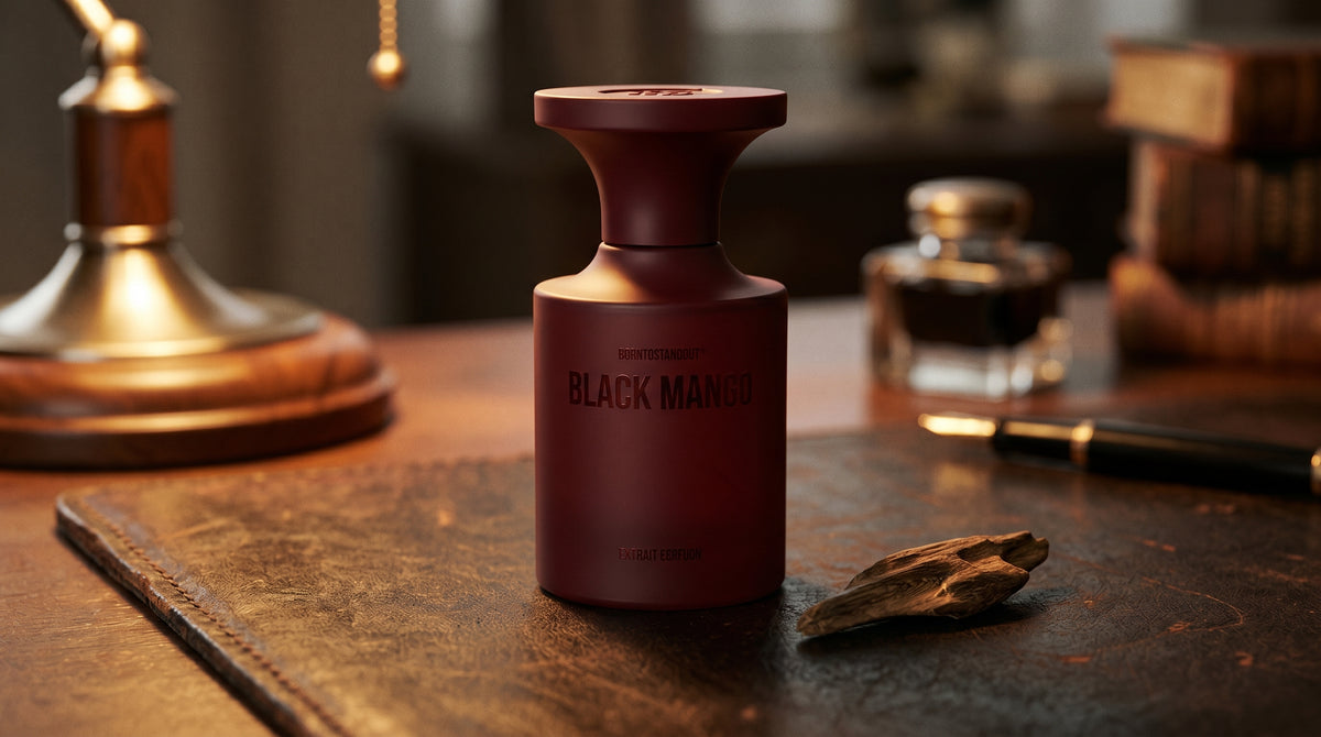 Borntostandout Black Mango Extrait Extreme on aged leather-topped desk with a single agarwood chip beside the bottle