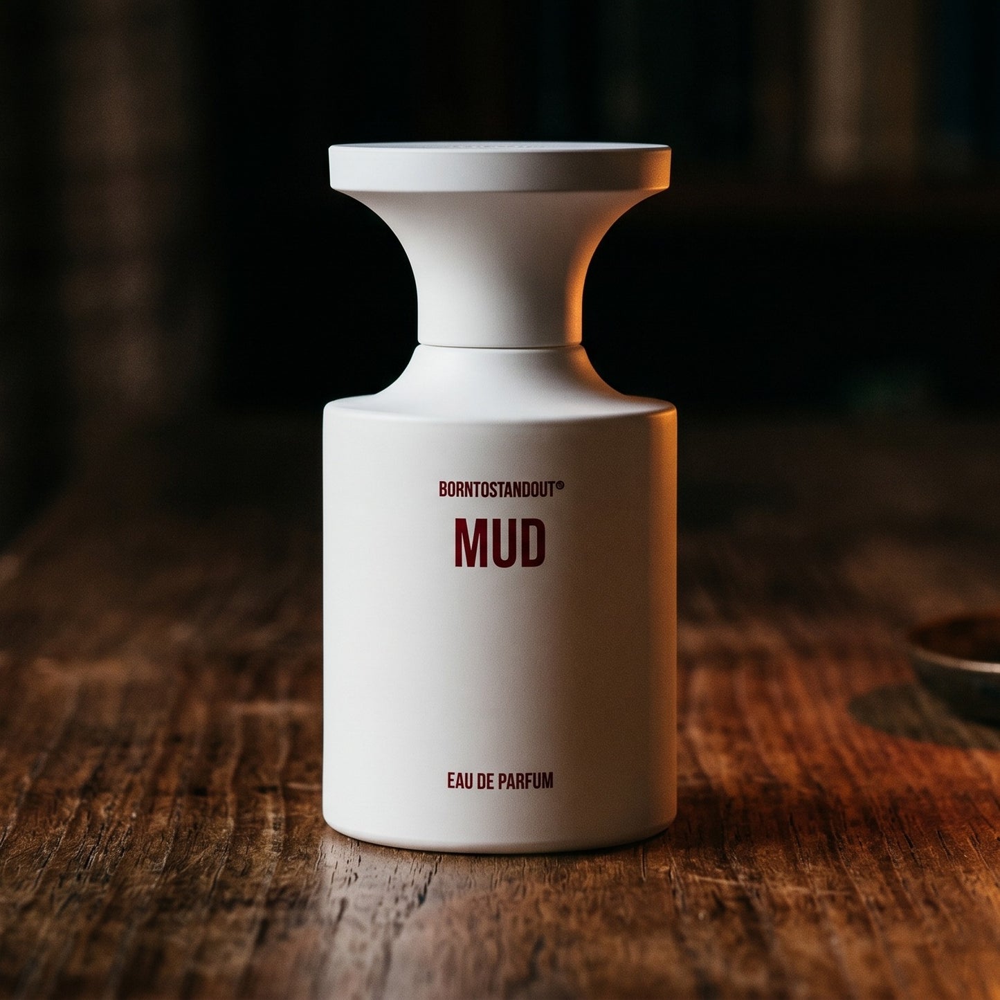 Borntostandout Mud EDP on walnut side table with a pair of lit votives beside the bottle