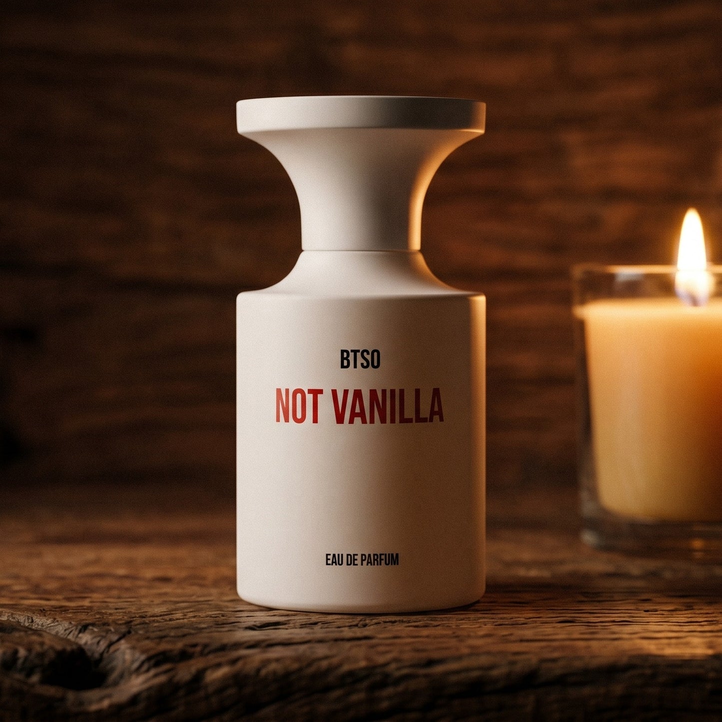 Borntostandout Not Vanilla EDP on rosewood surface with a squat brass candle flickering nearby