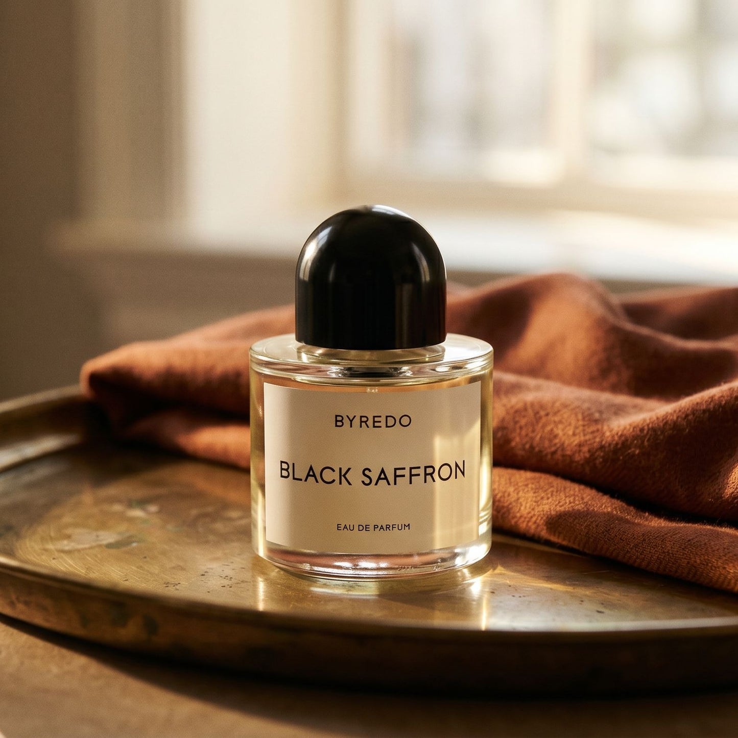 Byredo Black Saffron on brass-edged surface with a silk-wool wrap in burnt sienna