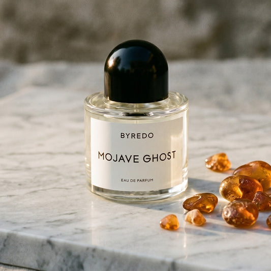 Byredo Mojave Ghost on cream stone with a scatter of honey-colored ambergris flakes