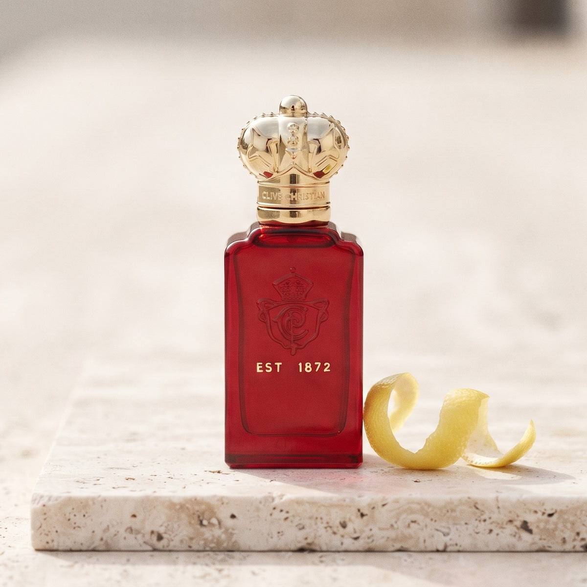 Clive Christian Crab Apple Blossom on pale travertine with a lemon peel curled beside the bottle
