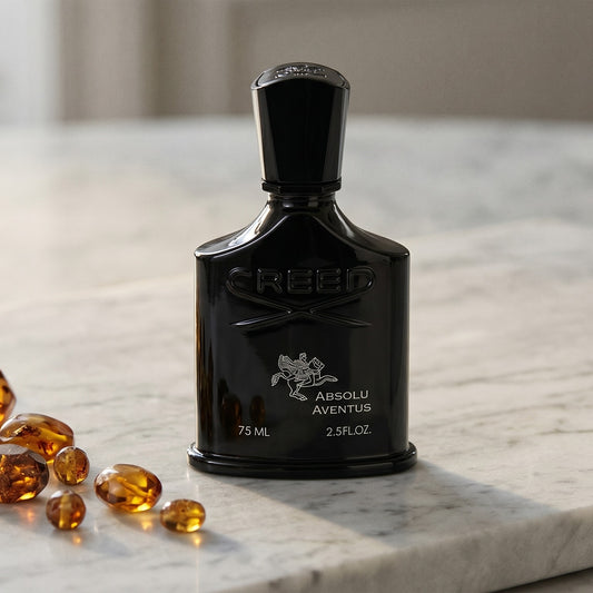 Creed Absolu Aventus on pale grey marble with amber resin beads scattered to one side