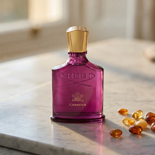 Creed Carmina on cream stone with a scatter of honey-colored ambergris flakes