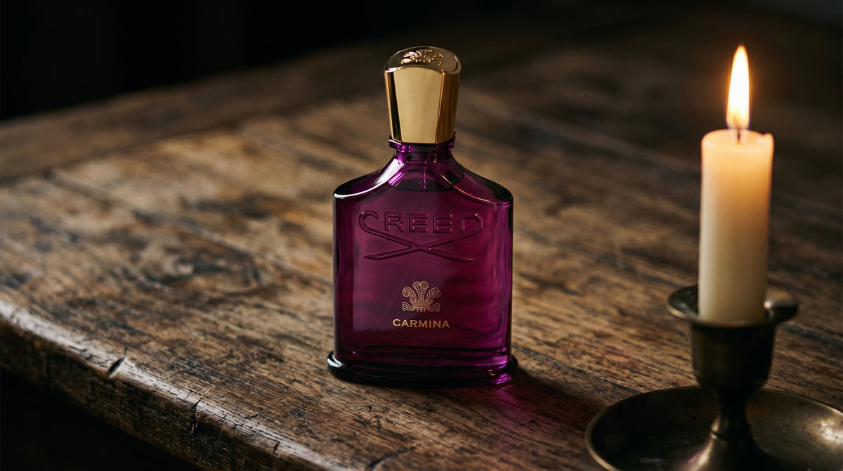 Creed Carmina on aged teak with a candle burning gently to frame-right