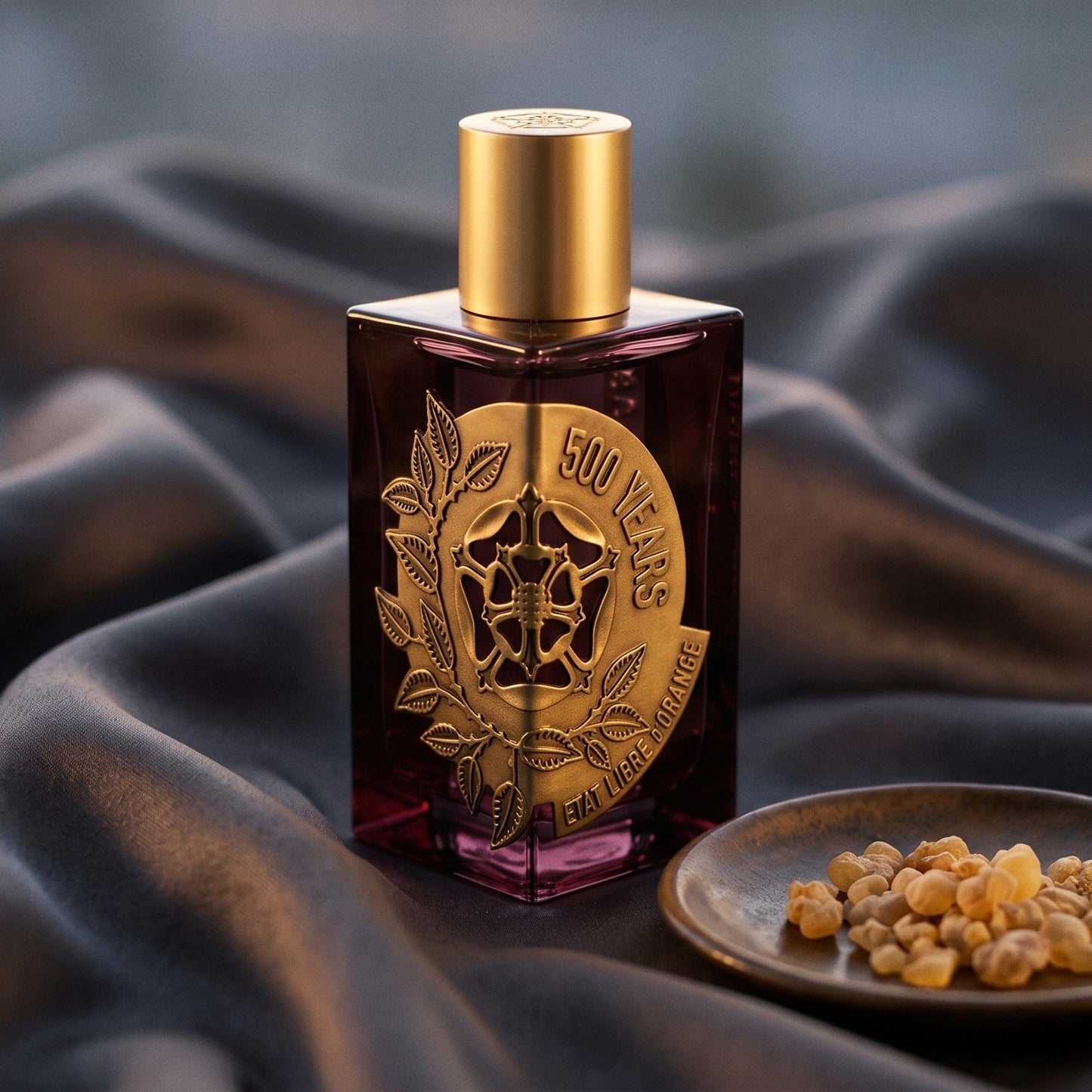 Etat Libre 500 Year EDP on charcoal raw silk with amber resin pieces near the bottle base