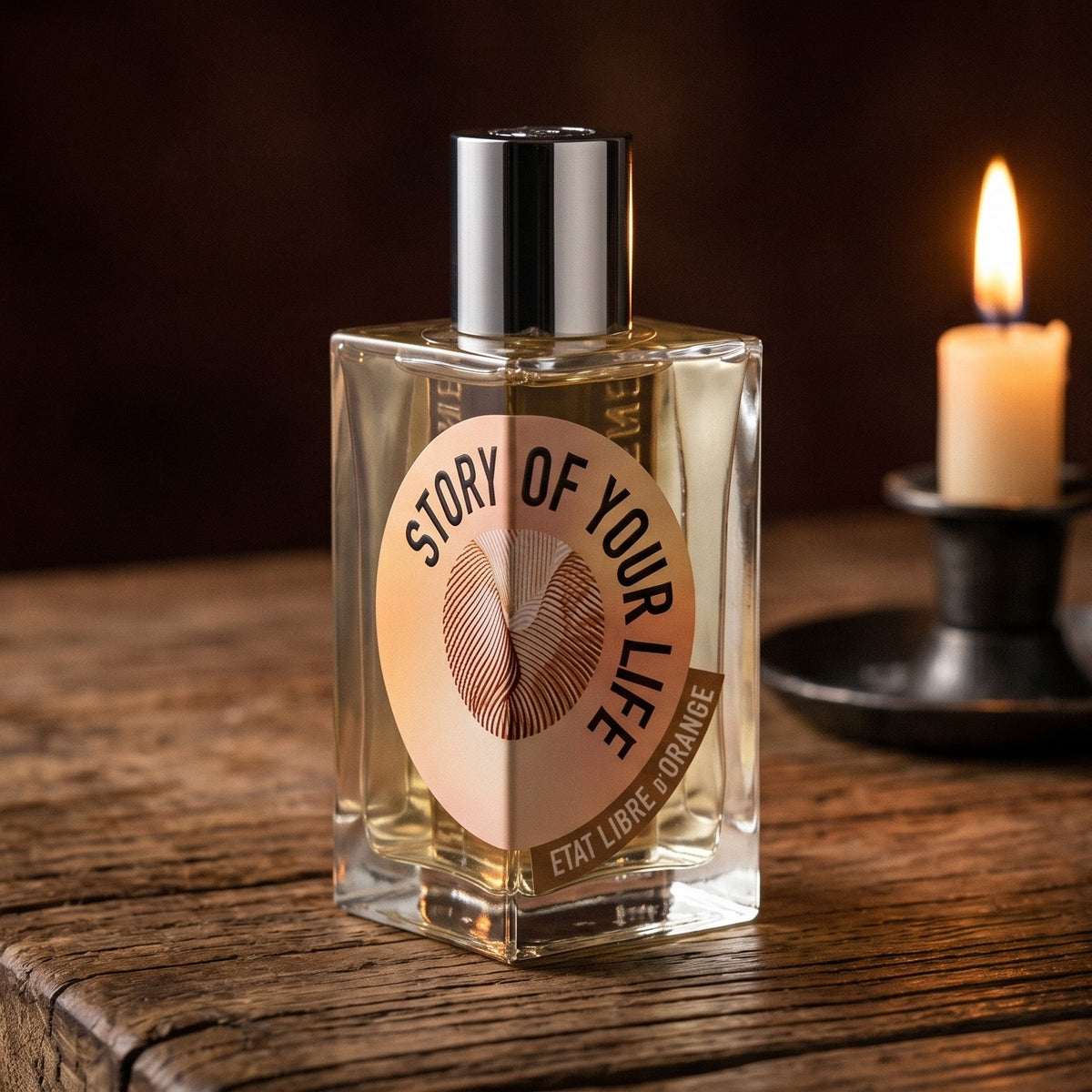 Etat Libre Story of Your Life on reclaimed oak surface with a glass hurricane lamp softly glowing