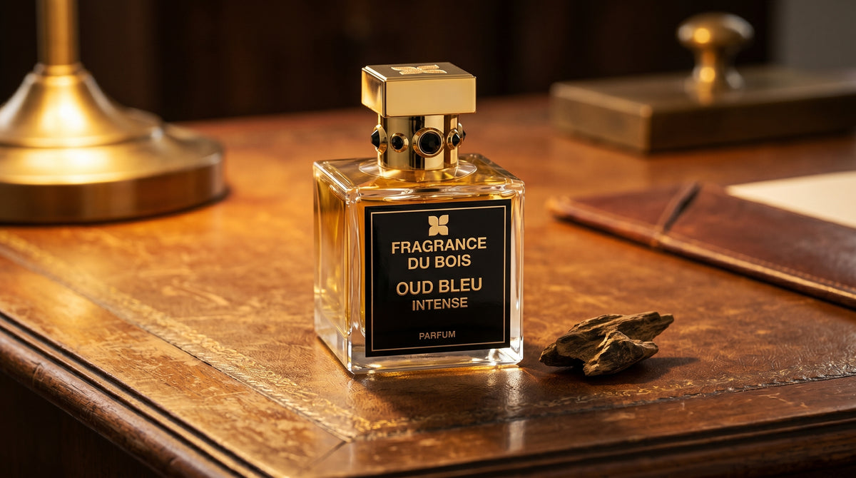 Fragrance du Bois Oud Bleu Intense on aged leather-topped desk with a single agarwood chip beside the bottle