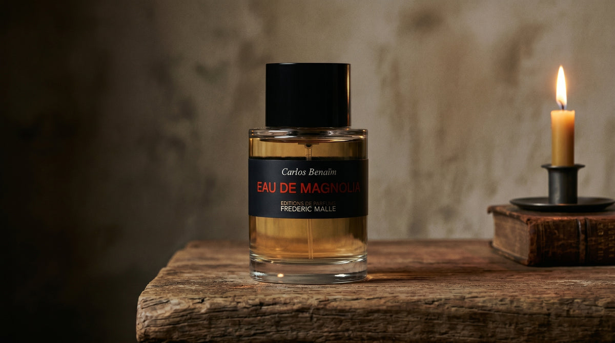 Frederic Malle Eau De Magnolia EDP on aged teak with a candle burning gently to frame-right