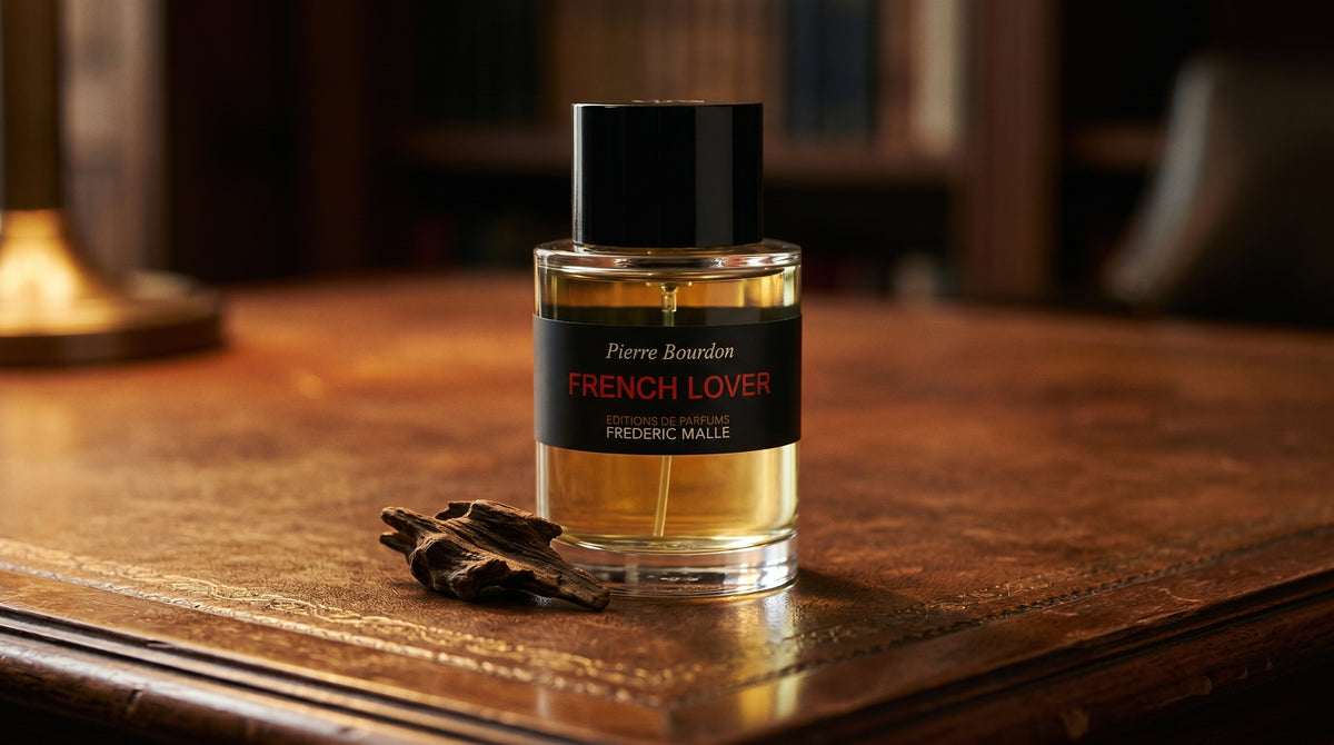 Frederic Malle French Lover EDP on aged leather-topped desk with a single agarwood chip beside the bottle