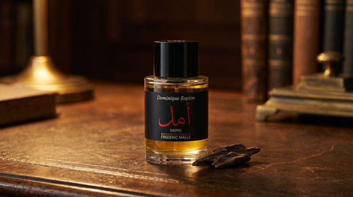 Frederic Malle Hope EDP on aged leather-topped desk with a single agarwood chip beside the bottle