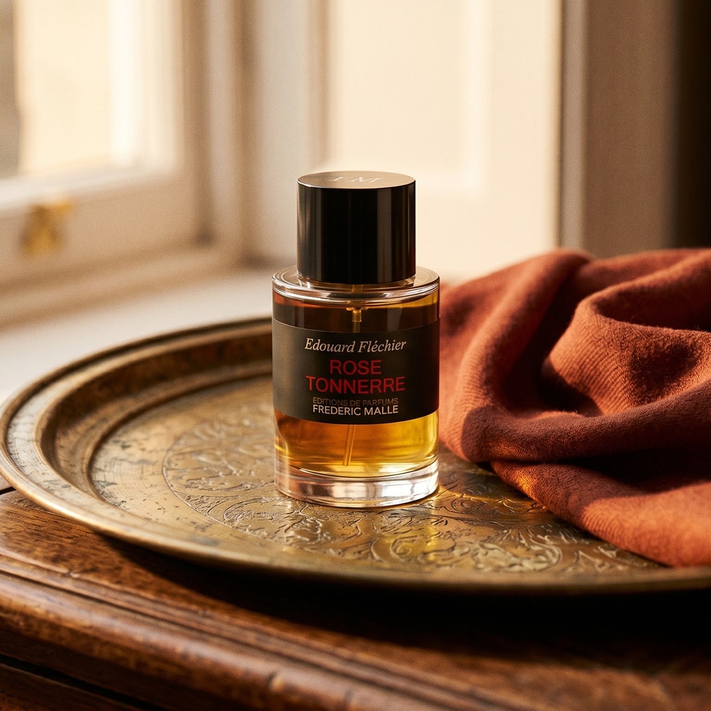 Frederic Malle Rose Tonnere EDP on brass-edged surface with a silk-wool wrap in burnt sienna
