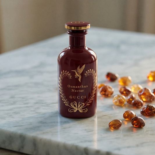 Gucci The Alchemist Garden Osmanthus Nectar EDP on cream stone with a scatter of honey-colored ambergris flakes