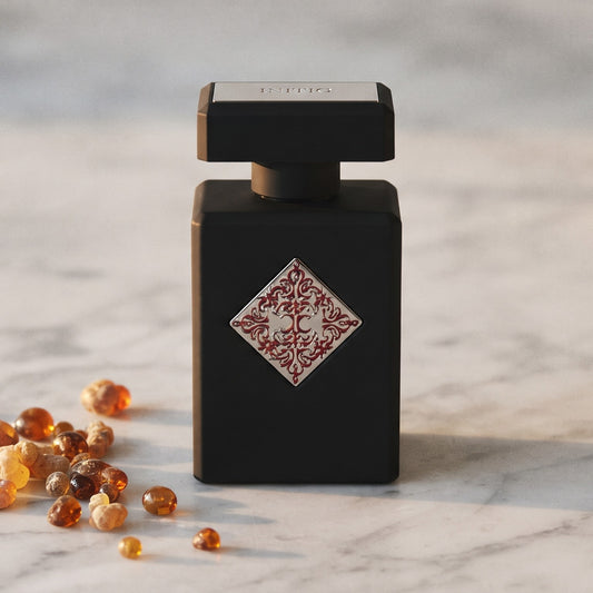 Initio Blessed Baraka EDP on pale grey marble with amber resin beads scattered to one side