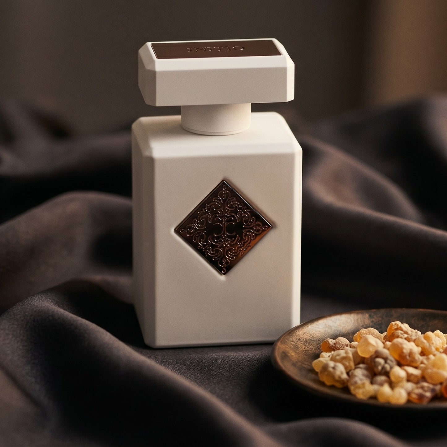 Initio Paragon on burnt-orange silk with smoldering agarwood on a stone dish
