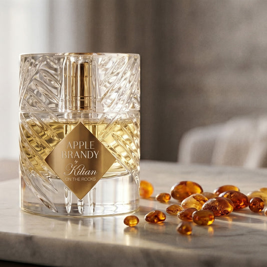 Kilian Apple Brandy on the Rocks on pale grey marble with amber resin beads scattered to one side