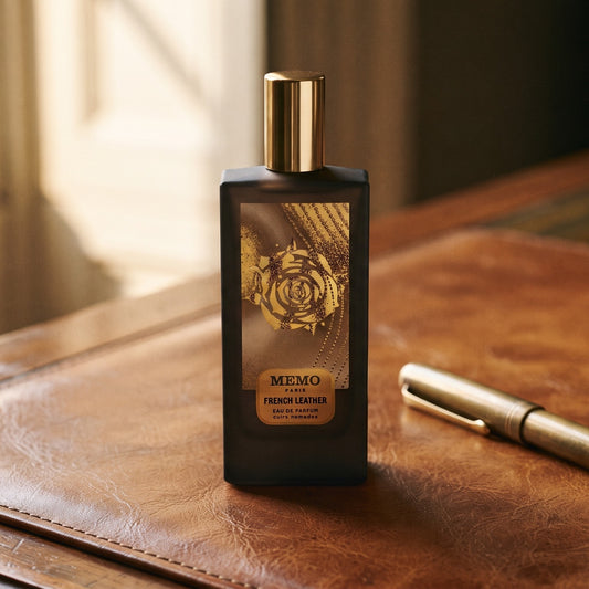 Memo Paris French Leather EDP on aged cognac-leather surface with a brass fountain pen resting beside the bottle