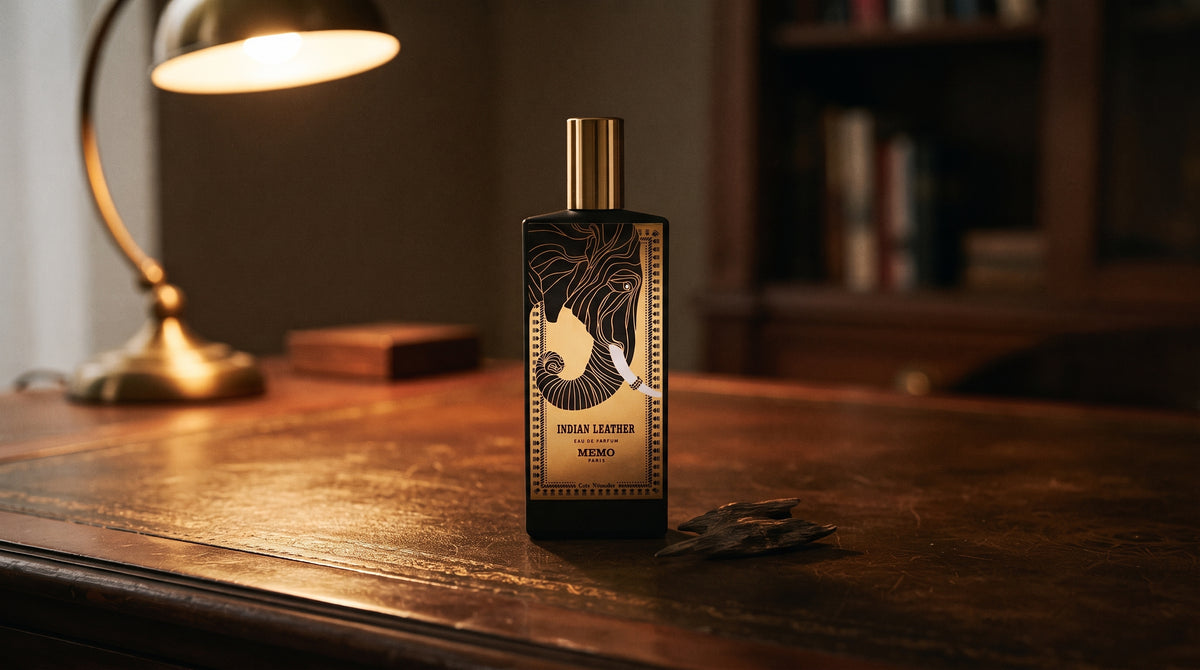 Memo Paris Indian Leather EDP on aged leather-topped desk with a single agarwood chip beside the bottle
