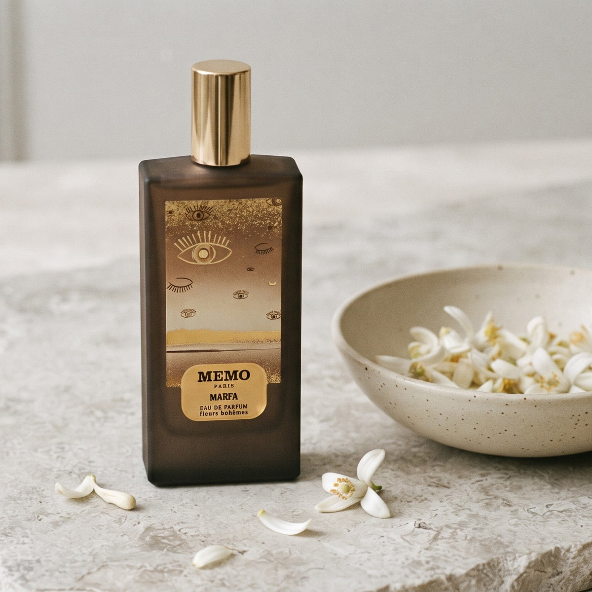Memo Paris Marfa EDP on pale stone with orange-blossom petals in a shallow bowl