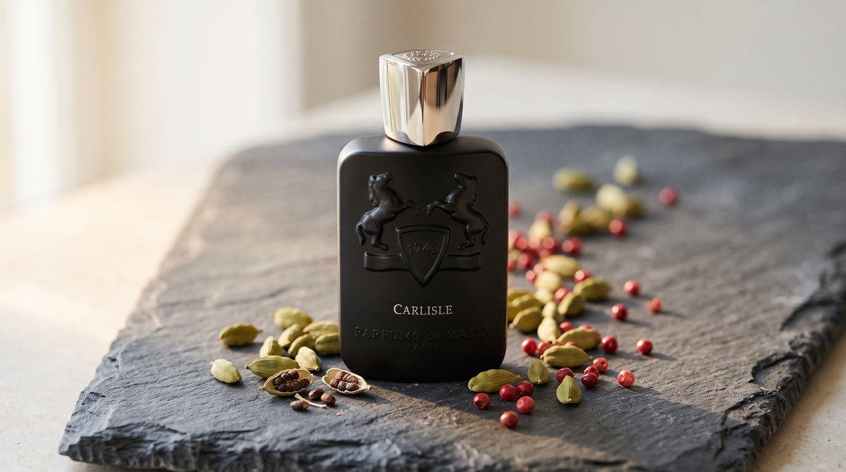 Parfums de Marly Carlisle EDP on dark grey stone slab with cardamom pods and pink peppercorns scattered
