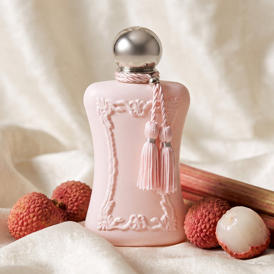 Parfums de Marly Delina EDP on cream silk with fresh lychees, one peeled, beside rhubarb stalks