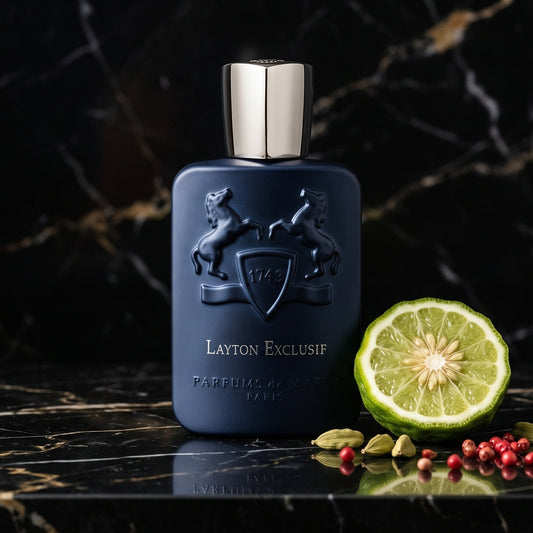 Parfums de Marly Layton Exclusif Parfum on black marble with a halved bergamot beside a few cardamom pods and pink peppercorns