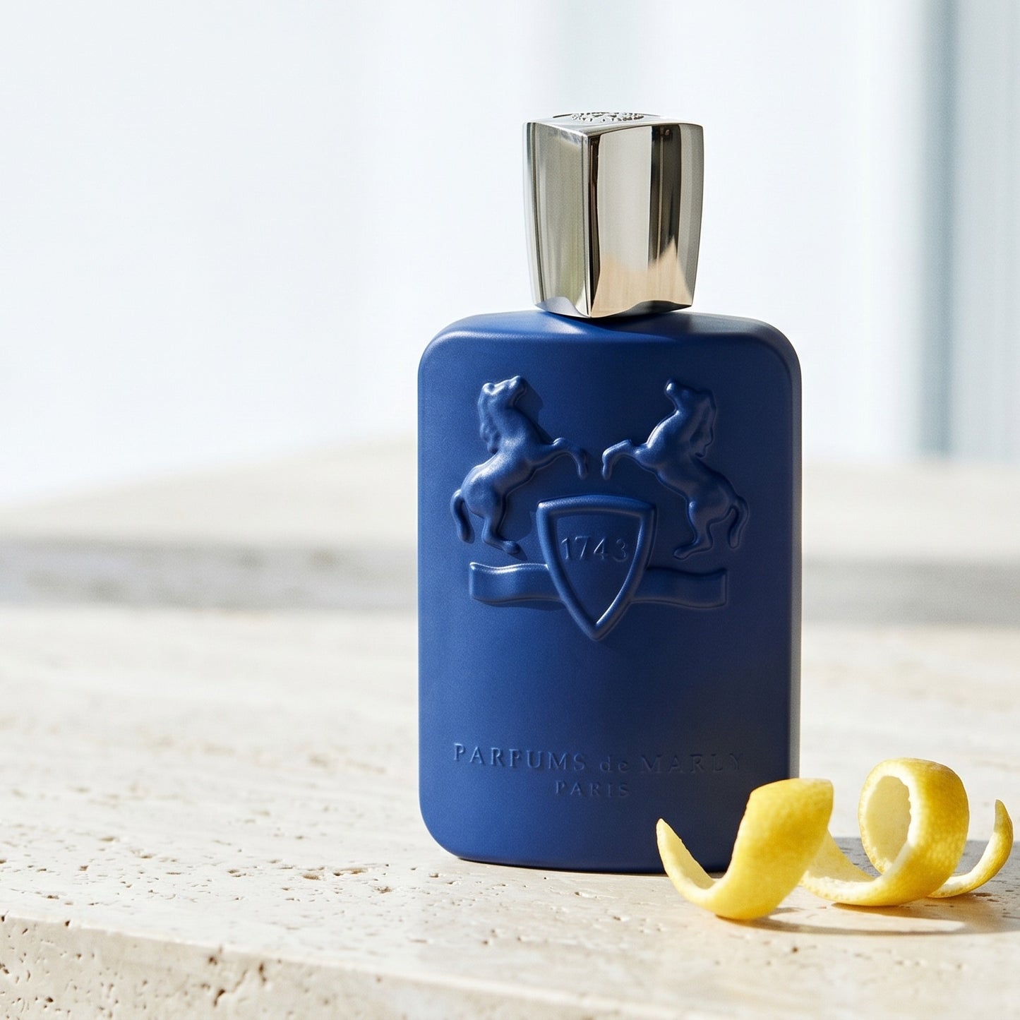 Parfums de Marly Percival EDP on ivory travertine with lime peel drizzled across the surface