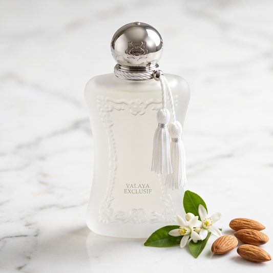 Parfums de Marly Valaya Exclusif EDP on white marble with a few whole almonds beside a sprig of orange blossom