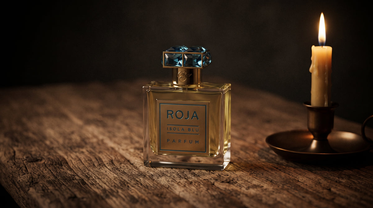 Roja Parfums Isola Blu Parfum on aged teak with a candle burning gently to frame-right