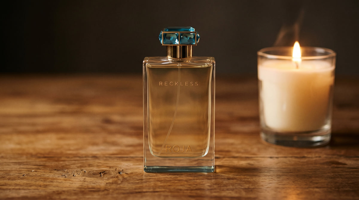 Roja Reckless Pour Femme EDP on aged teak with a candle burning gently to frame-right