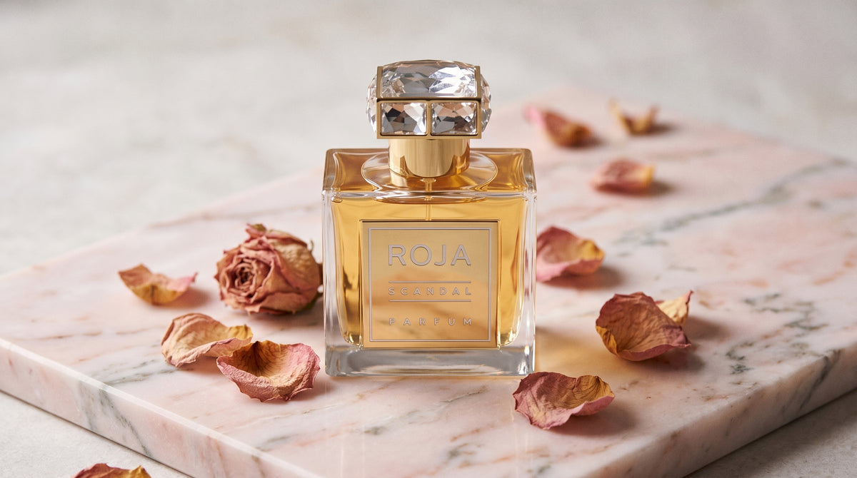 Roja Scandal Pour Femme Parfum on pale pink marble with dried rose petals scattered softly