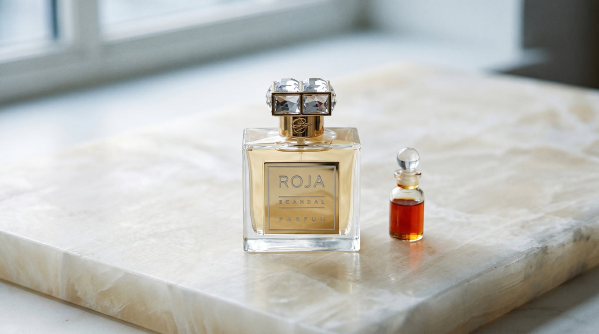 Roja Scandal Pour Femme Parfum on alabaster surface with rose attar in a tiny glass vial