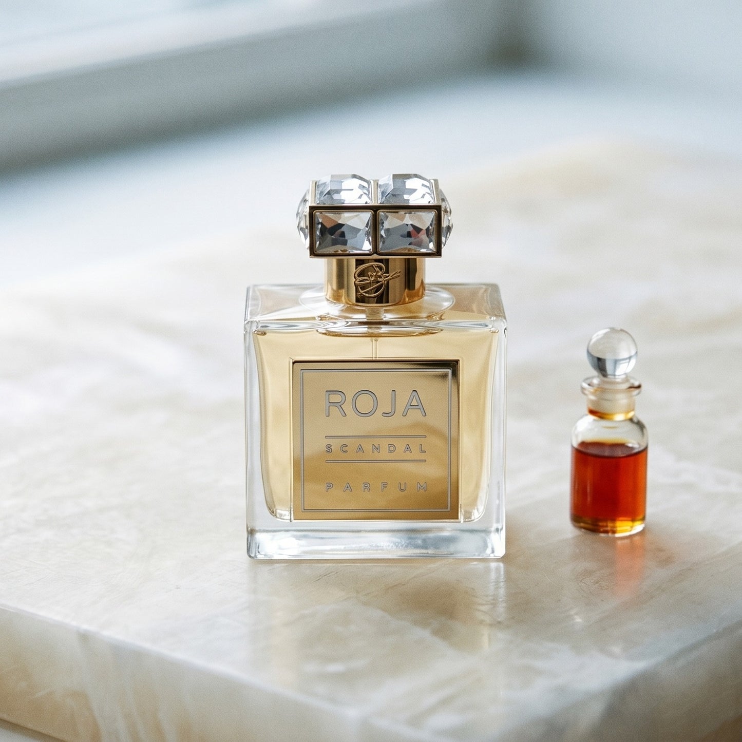 Roja Scandal Pour Femme Parfum on alabaster surface with rose attar in a tiny glass vial