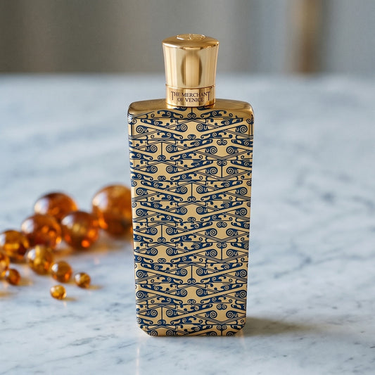 The Merchant of Venice Gold Regatta EDP on warm taupe marble with copal beads spilling from a small dish