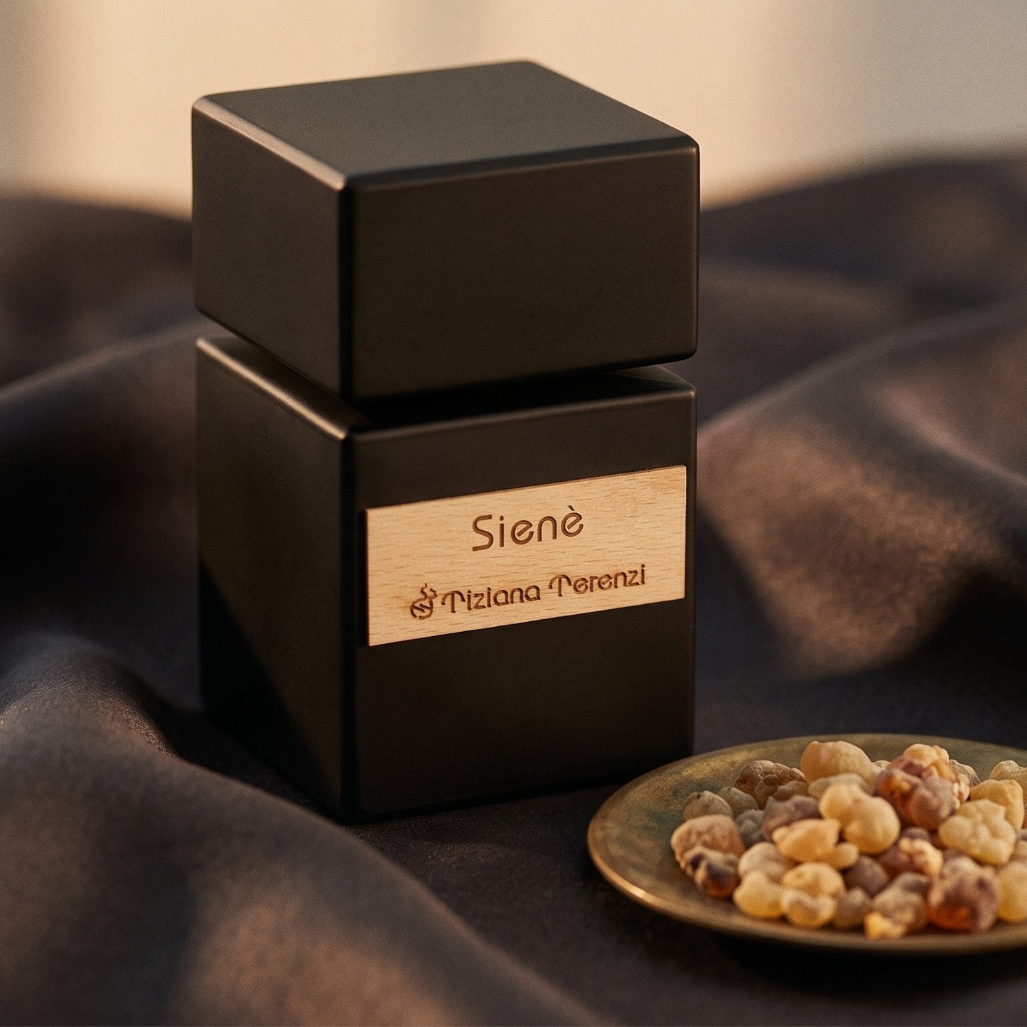 Tiziana Terenzi Siene EDP on burnt-orange silk with smoldering agarwood on a stone dish