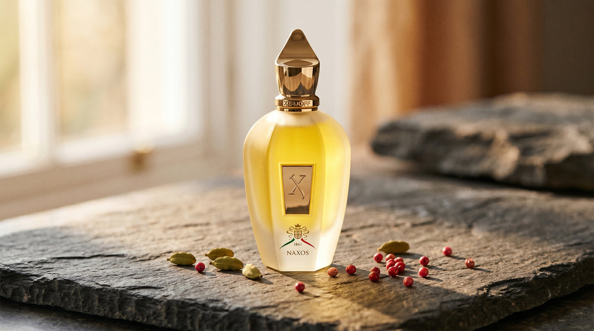 Xerjoff XJ 1861 Naxos on dark grey stone slab with cardamom pods and pink peppercorns scattered