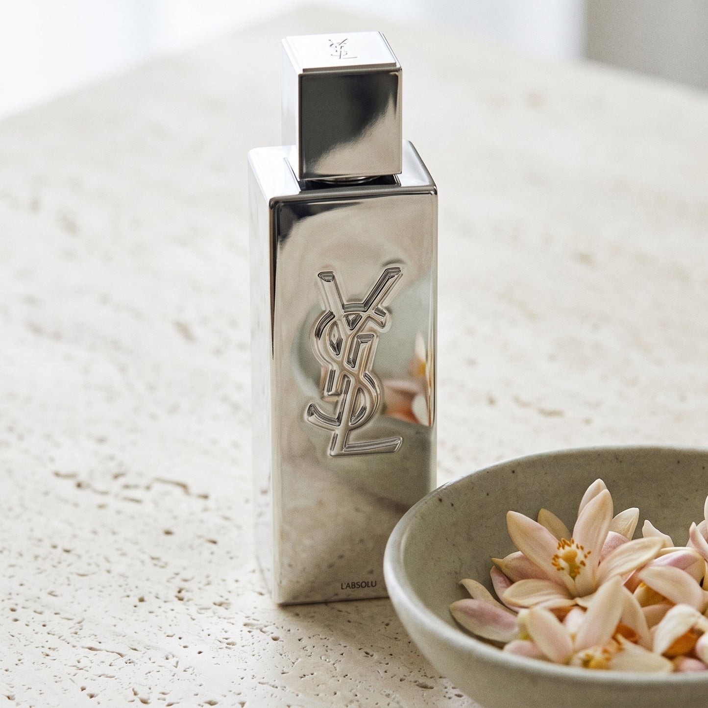 Yves Saint Laurent Myslf L Absolu Parfum on pale stone with orange-blossom petals in a shallow bowl