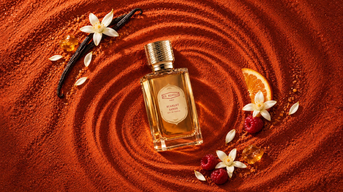 Ex Nihilo Scarlet Sands EDP bottle on swirled terracotta sand with raspberries, orange blossom, vanilla pods and a slice of orange