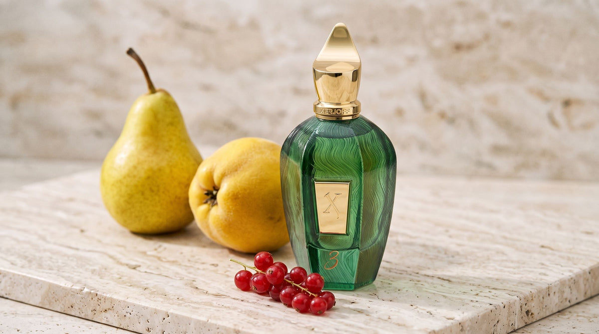 Xerjoff Three green UAE Exclusive bottle on pale travertine beside a ripe pear, a golden quince and fresh redcurrants