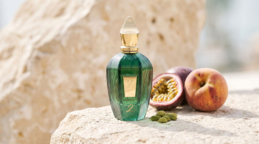 Xerjoff Two green UAE Exclusive bottle on pale limestone beside a halved passion fruit, a ripe peach and cardamom pods