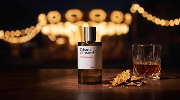 Maison Crivelli Tobacco Carnaval extrait de parfum on dark walnut with dried tobacco leaves and a glass of amber rum