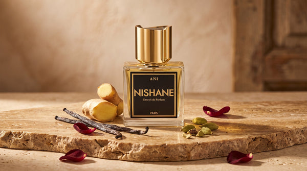 Nishane Ani extrait de parfum on travertine beside vanilla pods, cardamom, fresh ginger and red rose petals