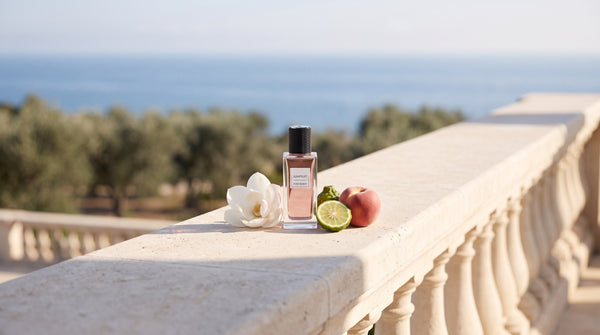 YSL Jumpsuit bottle on a limestone terrace ledge beside a white magnolia flower, a halved bergamot and a peach