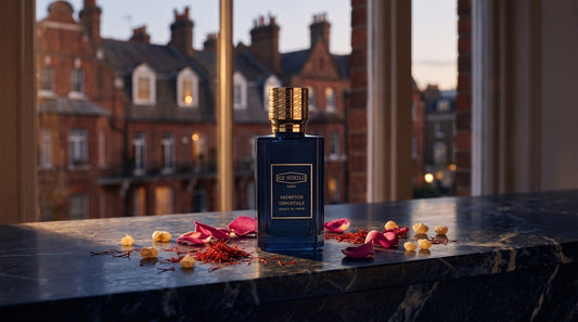 Ex Nihilo Brompton Immortals Extrait bottle on a dark navy marble ledge with saffron threads, rose petals and frankincense tears by a window onto red brick townhouses