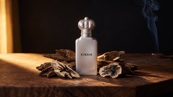Clive Christian Kinam Parfum, a frosted silver bottle with a crown cap, on dark walnut among chips of resinous agarwood with a ribbon of incense smoke